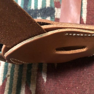 May include: Close-up of a brown leather belt with a stitched loop. The belt is folded over itself and the stitching is visible.