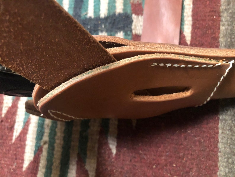 May include: Close-up of a brown leather belt with a stitched loop. The belt is folded over itself and the stitching is visible.