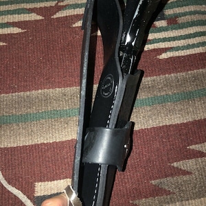 Peut inclure: Un &eacute;tui en cuir noir avec un motif cousu et une boucle argent&eacute;e. Un pistolet noir est &agrave; l'int&eacute;rieur de l'&eacute;tui.