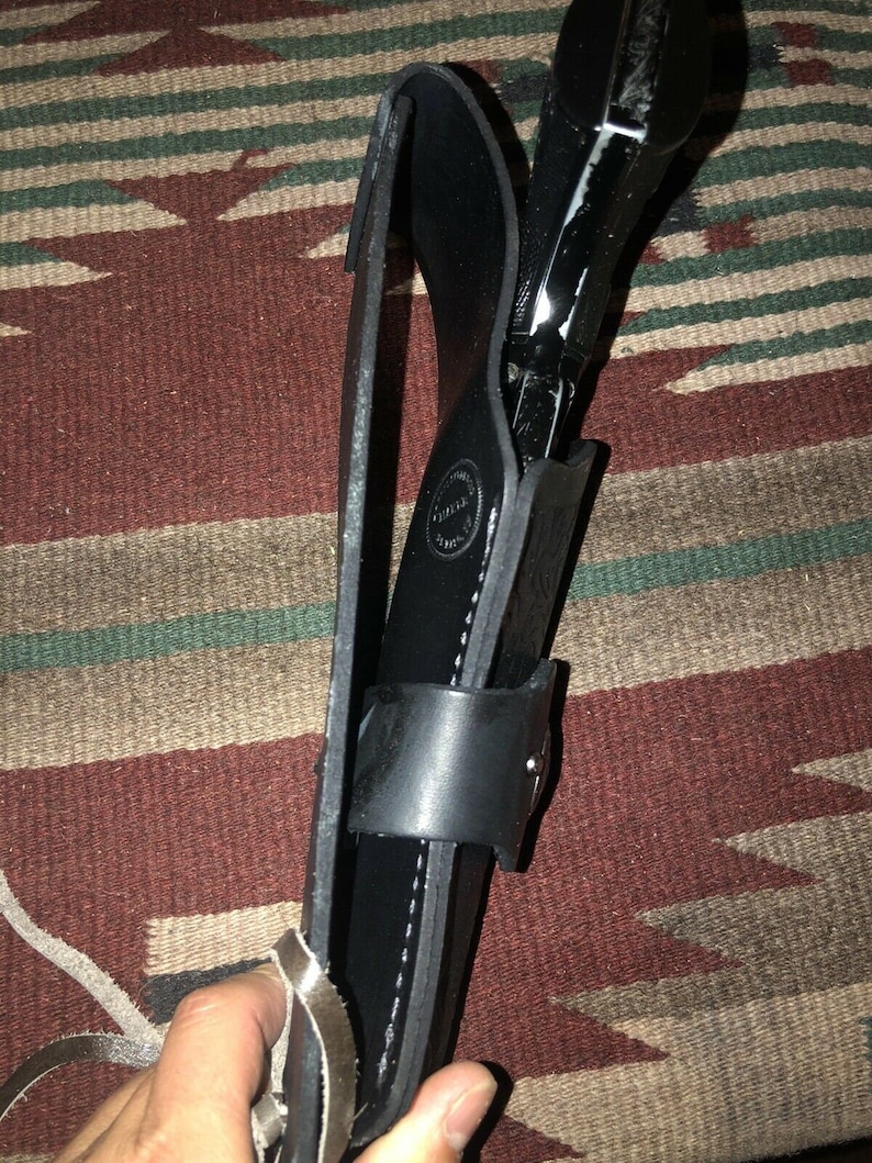 Peut inclure: Un &eacute;tui en cuir noir avec un motif cousu et une boucle argent&eacute;e. Un pistolet noir est &agrave; l'int&eacute;rieur de l'&eacute;tui.