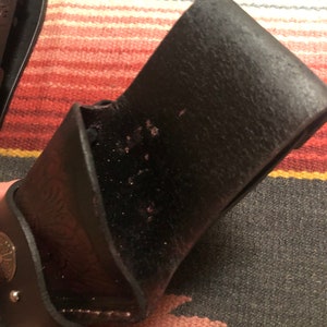 May include: A black leather holster with a decorative design. The holster has a flap that closes with a snap.