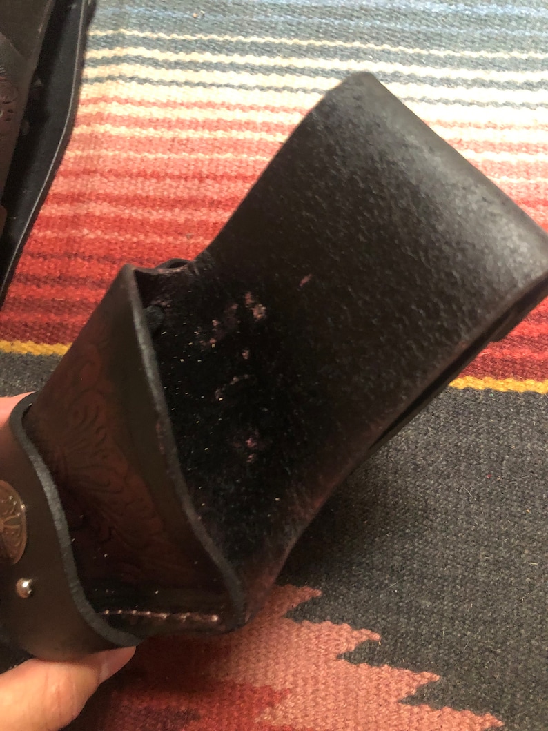 May include: A black leather holster with a decorative design. The holster has a flap that closes with a snap.