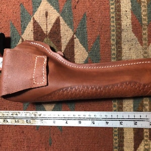 Op de afbeelding: Een bruine leren holster met een gestikt ontwerp en een wit stikdetail. De holster is 23 cm lang.