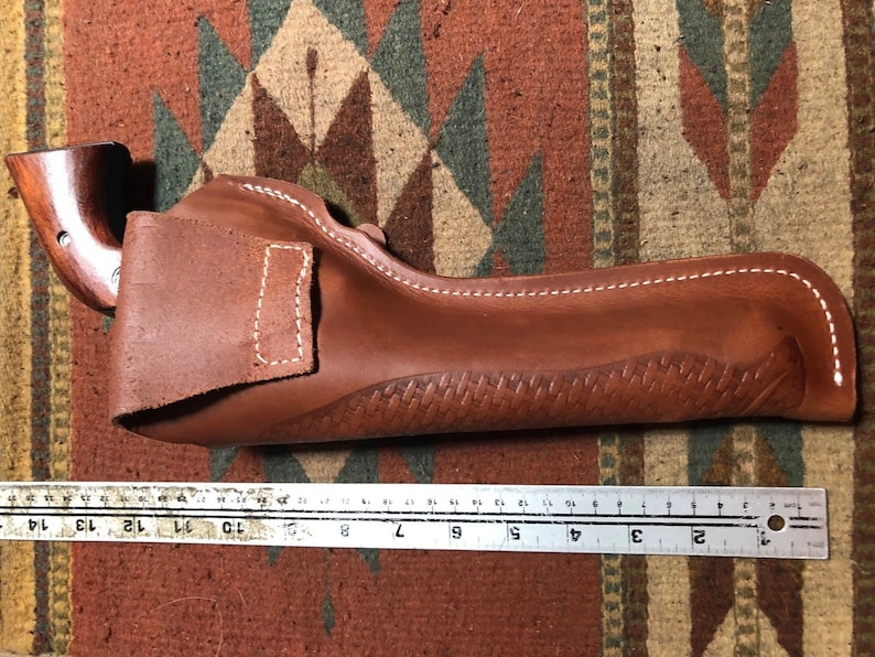 Op de afbeelding: Een bruine leren holster met een gestikt ontwerp en een wit stikdetail. De holster is 23 cm lang.