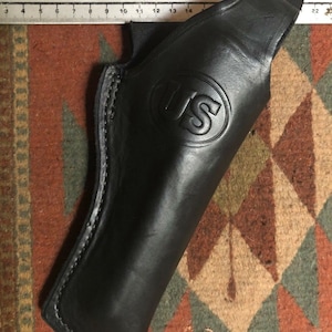 Pode incluir: Um coldre de couro preto com uma borda costurada e um logotipo dos EUA estampado na frente.