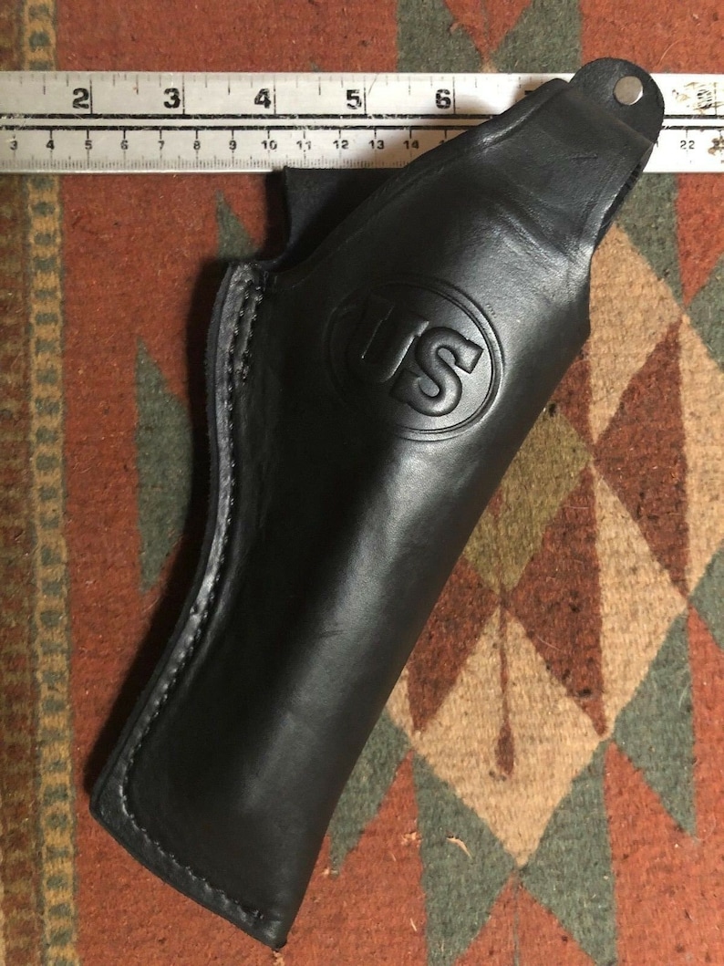 Pode incluir: Um coldre de couro preto com uma borda costurada e um logotipo dos EUA estampado na frente.