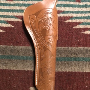 May include: A brown leather holster with a floral design. The holster has a white stitching detail around the edge.