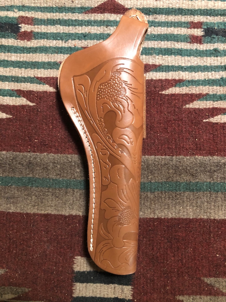 May include: A brown leather holster with a floral design. The holster has a white stitching detail around the edge.