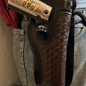 May include: A brown leather holster with a woven pattern, holding a silver and black handgun with gold horse head engravings.