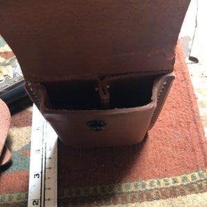 May include: A brown leather holster with two compartments and a snap closure. The holster is open and empty.