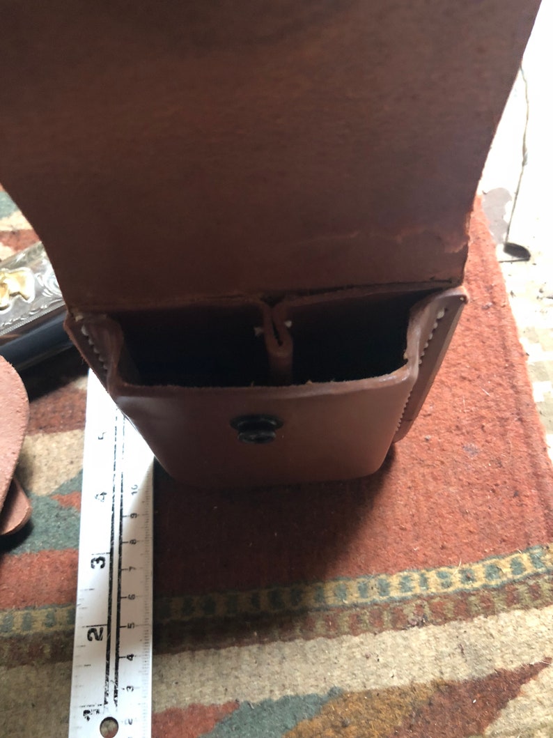 May include: A brown leather holster with two compartments and a snap closure. The holster is open and empty.