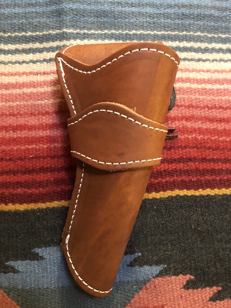 May include: A brown leather holster with white stitching. The holster is designed to hold a pistol.