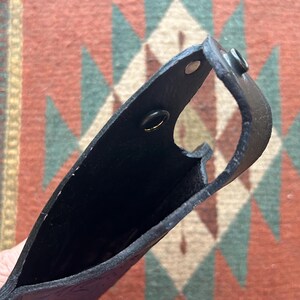 K&ouml;nnte beinhalten: Schwarzes Lederholster mit zwei Metalldruckkn&ouml;pfen. Das Holster ist offen und leer.