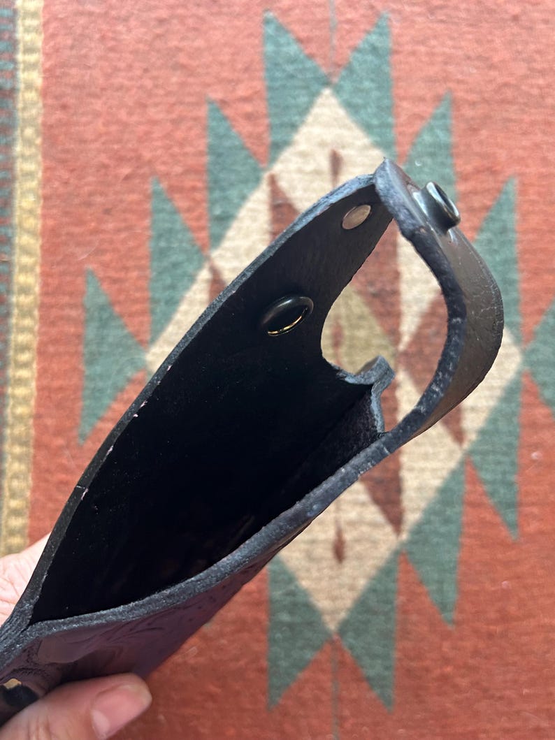 K&ouml;nnte beinhalten: Schwarzes Lederholster mit zwei Metalldruckkn&ouml;pfen. Das Holster ist offen und leer.