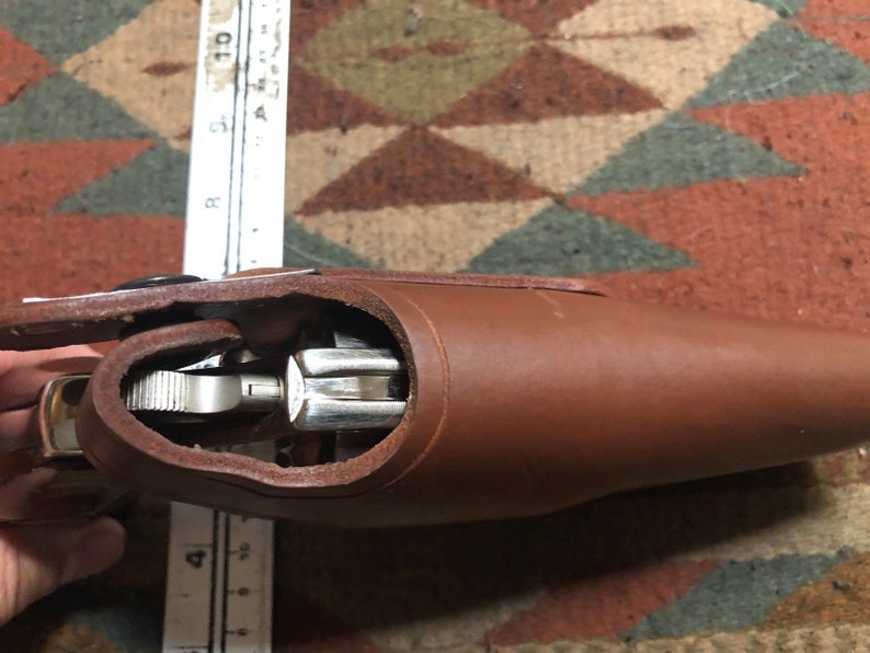 Puede incluir: Una funda de cuero marr&oacute;n con una pistola plateada en su interior. La funda est&aacute; abierta y el arma es visible.