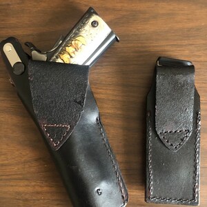 Puede incluir: Dos fundas de cuero negro para una pistola. Una funda est&aacute; abierta y tiene una pistola plateada con grabados dorados en su interior. La otra funda est&aacute; cerrada.