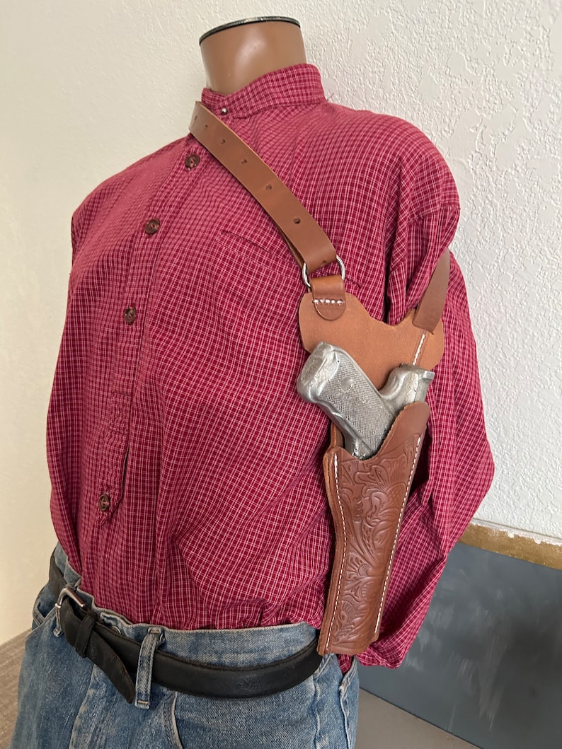 Puede incluir: Una funda de cuero marr&oacute;n con un dise&ntilde;o floral, que se lleva en el hombro de una persona, con una pistola plateada en su interior.