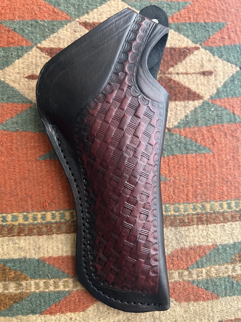 May include: A black leather holster with a burgundy basketweave pattern. The holster has a curved shape and a loop at the top. The stitching is visible along the edges. The holster is designed to hold a firearm.