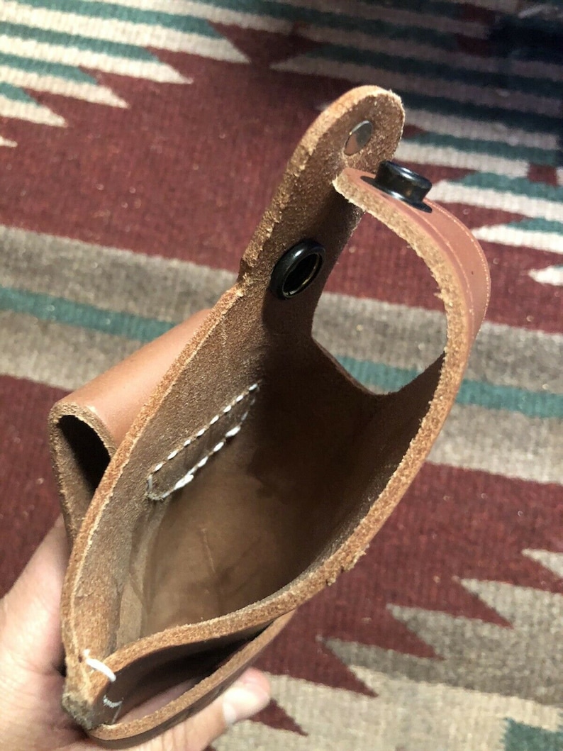 Op de afbeelding: Een bruine leren holster met een gestikte naad en drie metalen drukknopen. De holster is open en leeg.