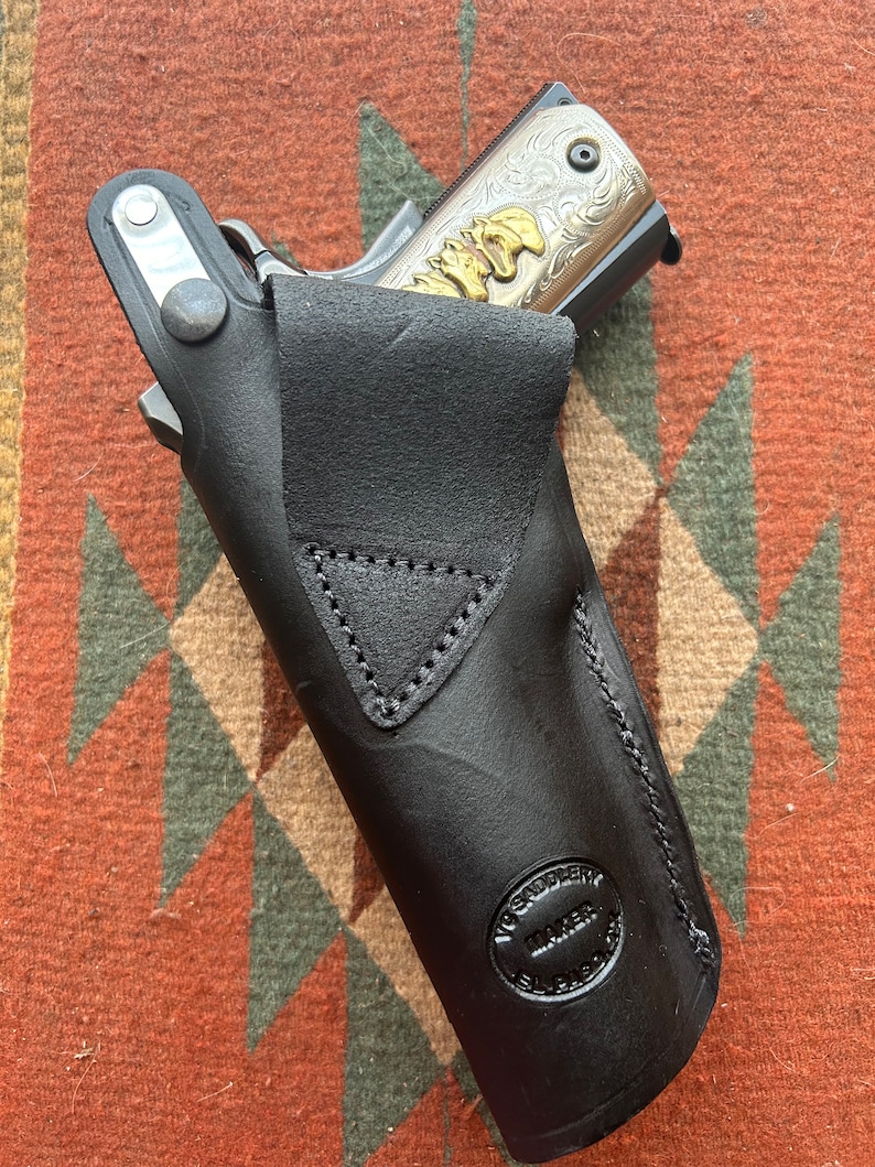 May include: A black leather holster with a silver snap and a "V. Saddlery Maker El Paso" stamp. A silver and gold engraved handgun is partially visible inside the holster.