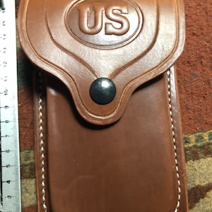 May include: A brown leather phone case with white stitching and a US emblem on the front.