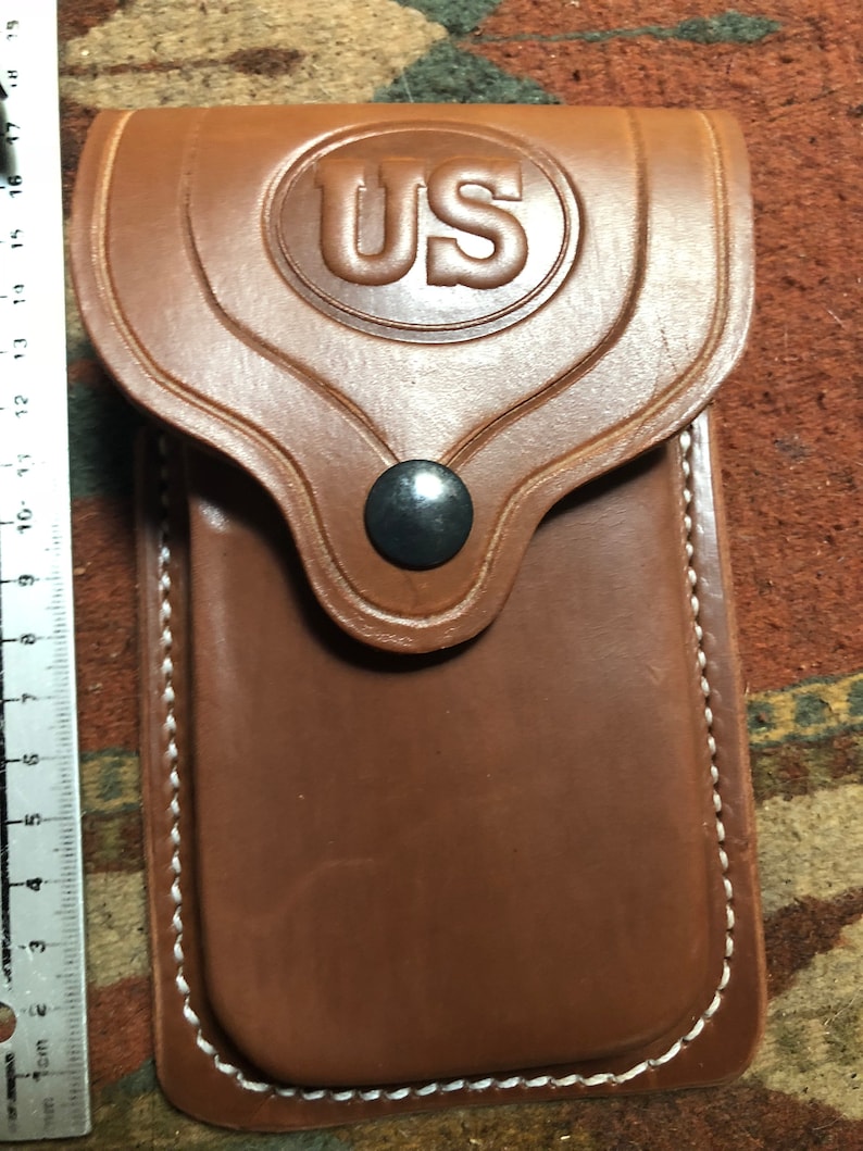 May include: A brown leather phone case with white stitching and a US emblem on the front.