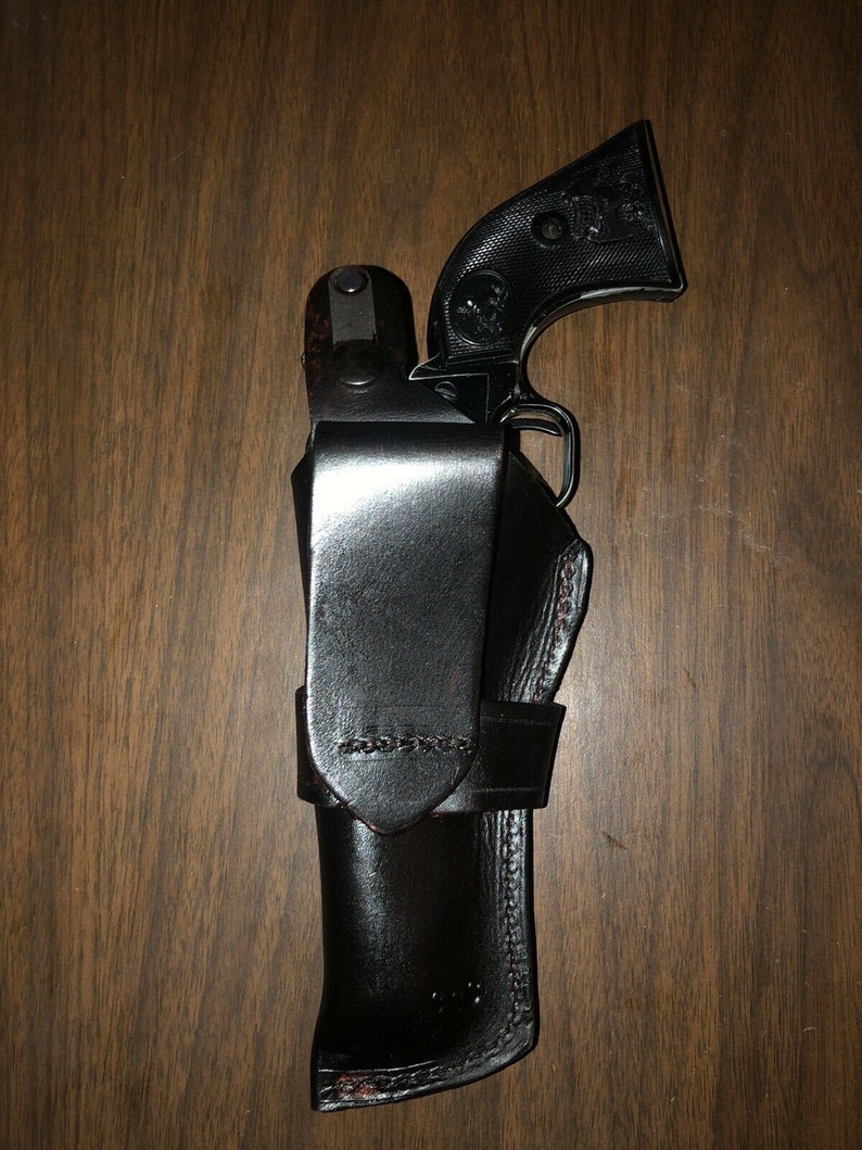 May include: A black leather holster with a black handgun inside. The holster has a flap that covers the gun and a belt loop.