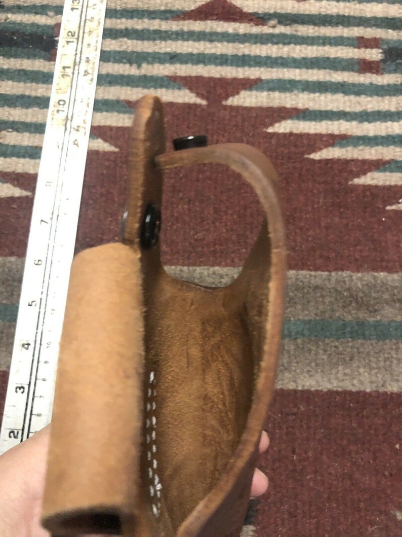 Op de afbeelding: Een bruine leren holster met een gestikte naad en een drukknopsluiting. De holster is open en leeg.