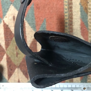 May include: Close-up of the inside of a black leather holster. The holster is made of thick leather and has a smooth finish. The inside of the holster is lined with a soft material.