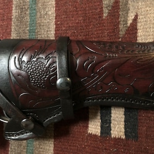 Puede incluir: Una funda de cuero marr&oacute;n con intrincados detalles florales. La funda est&aacute; dise&ntilde;ada para sostener una pistola y tiene un bucle para el cintur&oacute;n.