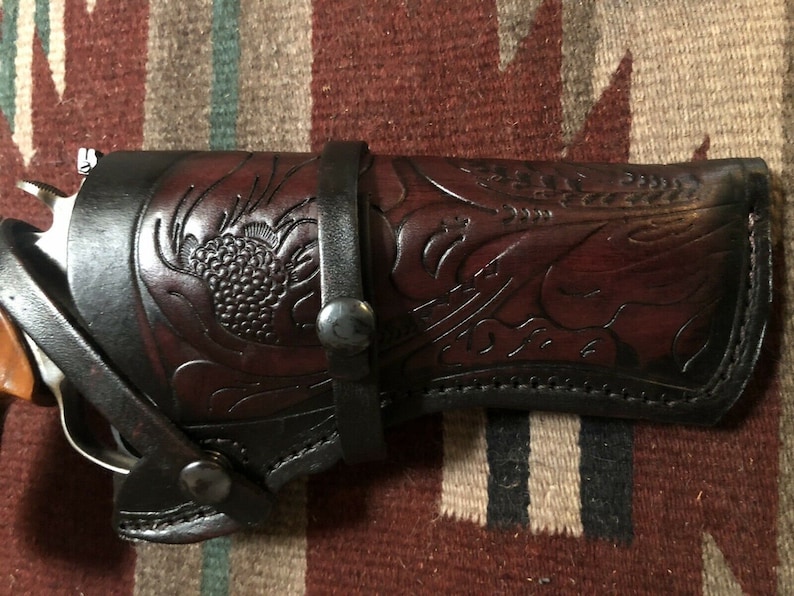 Puede incluir: Una funda de cuero marr&oacute;n con intrincados detalles florales. La funda est&aacute; dise&ntilde;ada para sostener una pistola y tiene un bucle para el cintur&oacute;n.