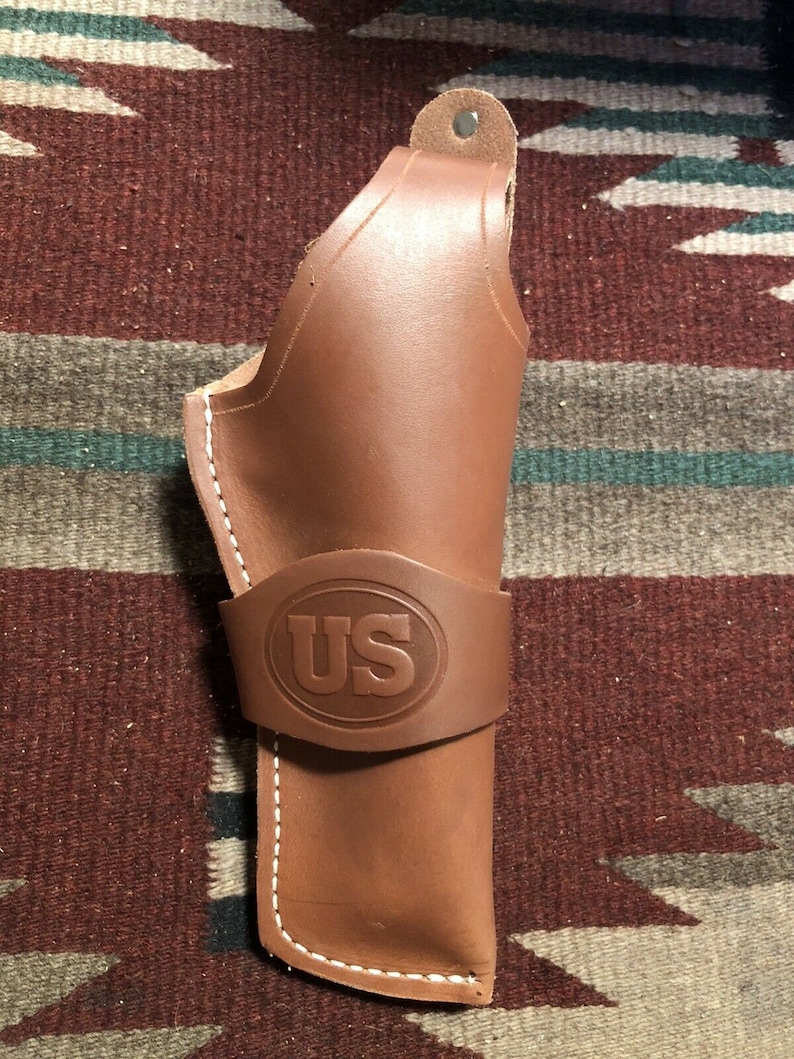 Op de afbeelding: Een bruine leren holster met witte stiksels en een US-logo dat op de voorkant is gegraveerd.