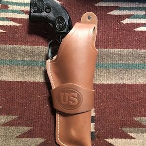 May include: A brown leather holster with a US logo and a black revolver inside.