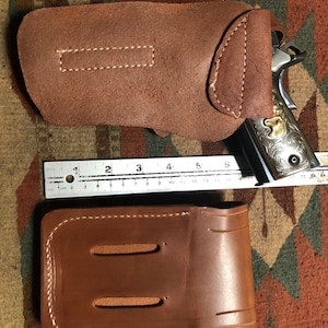 May include: Two brown leather holsters with white stitching. The holster on the top is designed to hold a gun. The holster on the bottom has two slots for carrying other items.