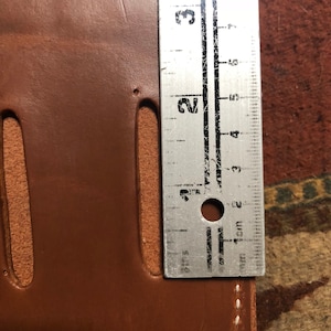May include: A brown leather wallet with a white stitch detail and a ruler measuring 3 cm in length.