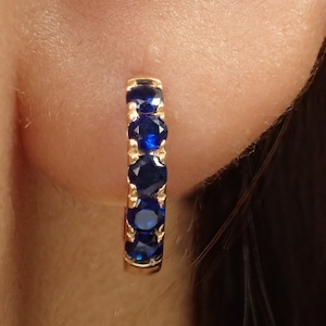 Può includere: Orecchini a cerchio in oro con cinque pietre blu.