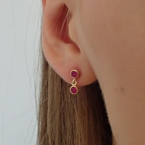 Pode incluir: Um par de brincos de ouro com duas pequenas pedras redondas de cor vermelha penduradas em cada brinco.