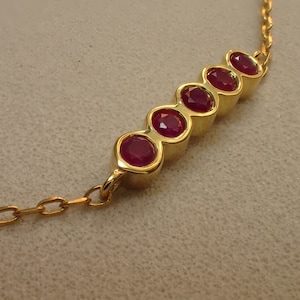 May include: A gold chain necklace with a row of six red gemstones set in gold.