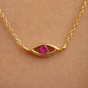 Könnte beinhalten: Eine goldene Kettenkette mit einem kleinen, augenförmigen Anhänger mit einem rosafarbenen Edelstein.