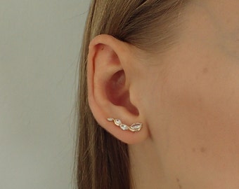May include: A gold ear cuff with five clear, oval-shaped stones set in a curved design.