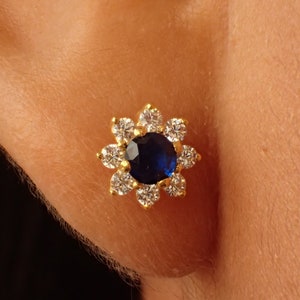 May include: Gold flower-shaped earring with a blue gemstone in the center and smaller clear gemstones around it.