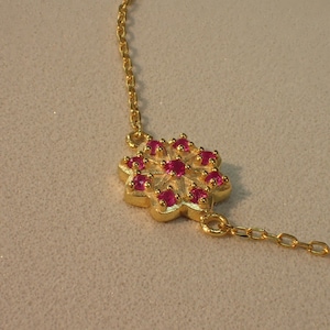May include: A gold chain necklace with a pink flower pendant. The flower has a detailed design and is adorned with small pink gemstones.