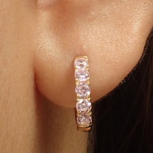 Może przedstawiać: Złote kolczyki koła z rzędem różowych cyrkonii.