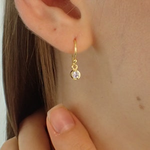 May include: Gold hoop earrings with a small clear stone dangling from the bottom.