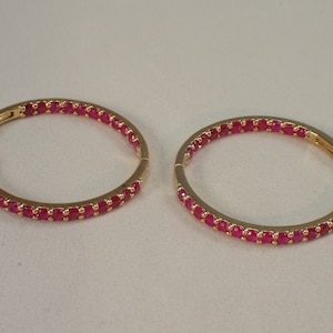 Könnte beinhalten: Ein Paar goldene Creolen mit einer Reihe kleiner, leuchtend rosa Edelsteine ​​am Rand.
