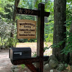 Puede incluir: Un poste de buzón de madera rústica con un buzón negro. El poste tiene un letrero con el número 399 y una estrella. Un segundo letrero dice "Woodworking Entity Custom Woodwork Rustic Handmade Furniture."