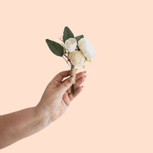 May include: A small bouquet of white sola flowers with green leaves, tied with twine, held in a hand.