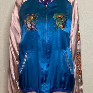 Könnte beinhalten: Eine blaue und rosafarbene Satin-Bomberjacke mit Stickereien auf Vorder- und Rückseite. Die Jacke hat einen Reißverschluss und gerippte Bündchen und einen Kragen.