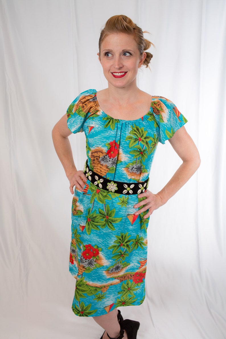 Puede incluir: Vestido turquesa con estampado tropical con palmeras, veleros y flores. El vestido tiene mangas cortas y est&aacute; ce&ntilde;ido a la cintura con un cintur&oacute;n negro adornado con detalles florales blancos y conchas. El vestido llega a las rodillas.