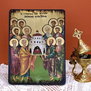 May include: A hand-painted icon depicting the Holy Apostles with a gold background and a wooden frame. The icon features a scene of the apostles carrying a small building with a red roof. The text on the icon reads "Η συναξις των αγιων δωδεκα αποστολων".